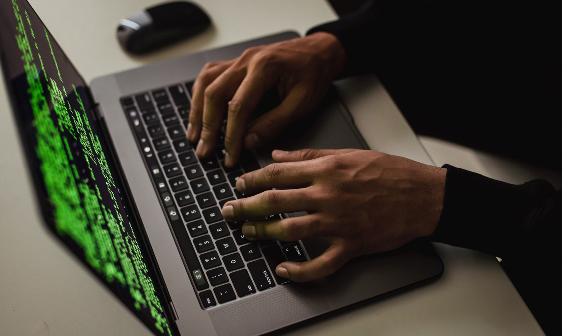 Hands typing on a laptop with green code on screen