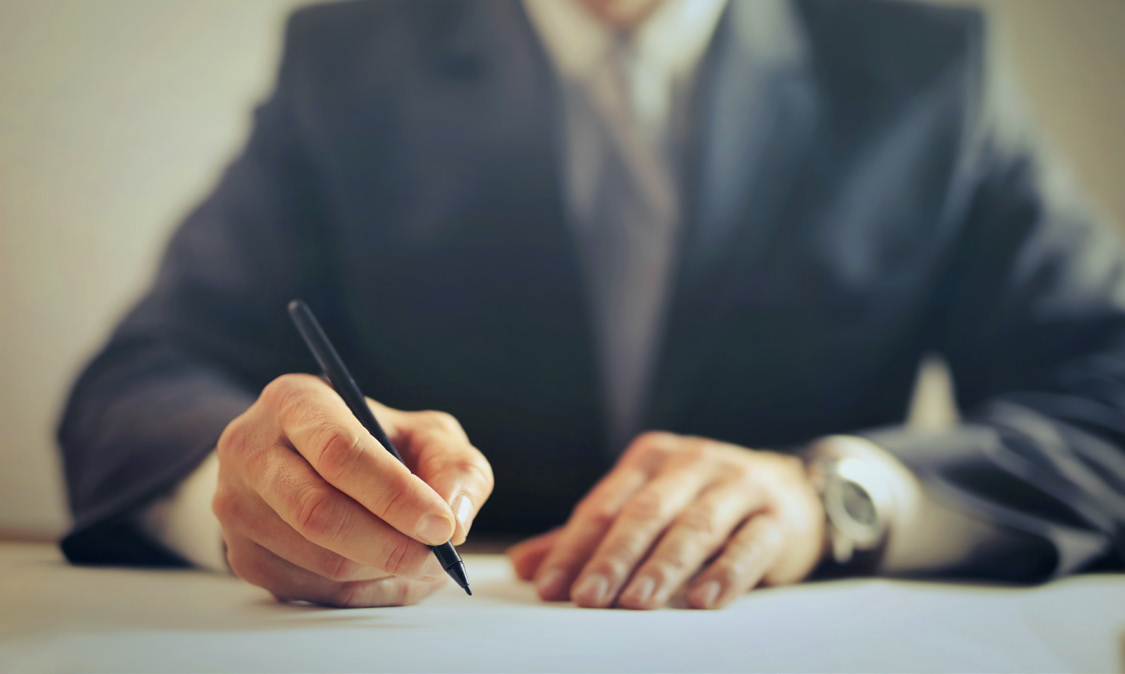 Executive in a suit signing a document with a pen