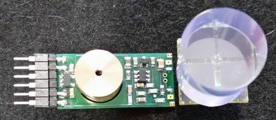 Photograph of a SiPM readout board with a clear scintillator crystal cylinder beside it.