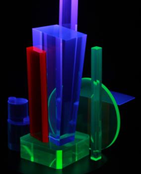 Plastic scintillator pieces in several shapes glowing blue, green, and red under stimulation.