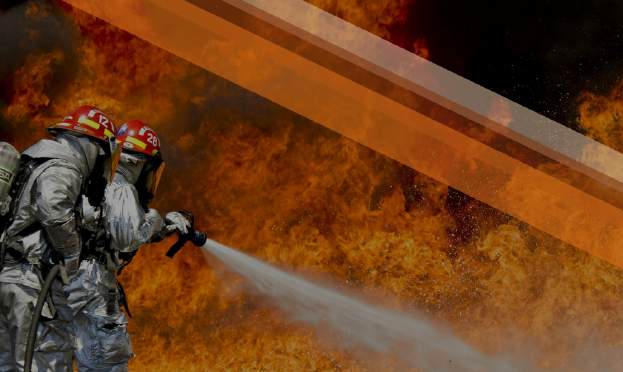 Firefighters directing water at an advancing wall of flame